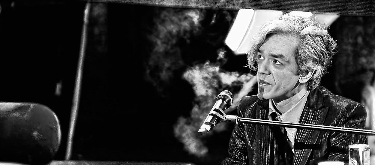 Black and white photograph of Morgan singing at the piano on stage, smoke drifting behind him